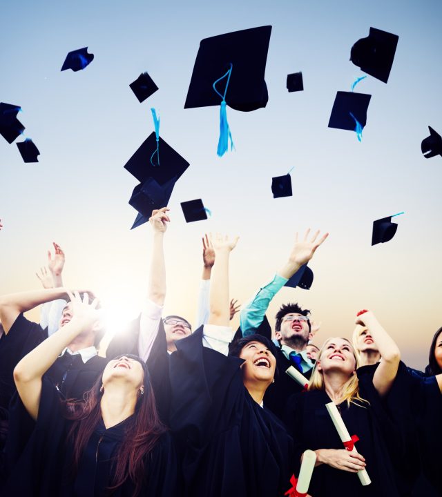 A group of  graduates throwing their graduation caps into the air.  They are smiling and cheering as they look up at the hats.